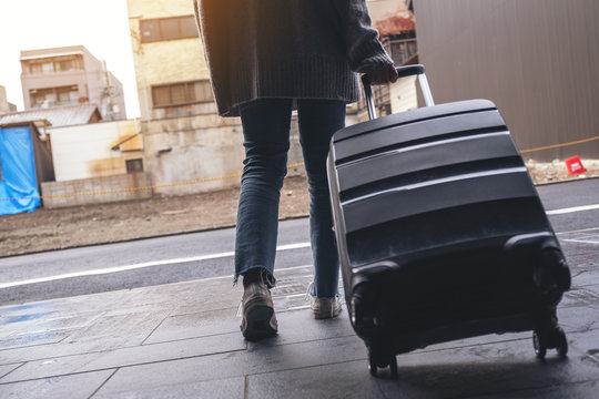 Closeup image of a woman walking while traveling and dragging a black baggage in the outdoors