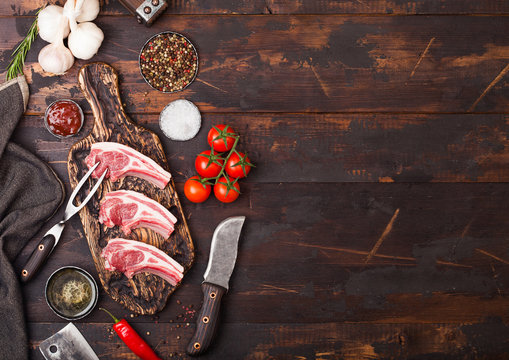 Fresh raw butchers lamb beef cutlets on chopping board with vintage meat fork and knife on wooden background.Salt, pepper and oil with tomatoes and garlic and barbeque sauce. Space for text