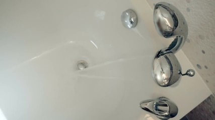 A beautiful faucet with a shower head is built into the corner of the bath, a hand presses the handle and water starts to flow from the tap in to the bath. Top view. Macro. Closeup. Slow mo, slo mo - Powered by Adobe