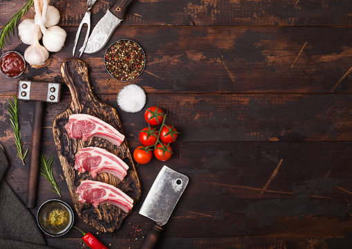 Fresh raw butchers lamb beef cutlets on chopping board with vintage meat hatchet and hammer on wooden background.Salt, pepper and oil with tomatoes and garlic and barbeque sauce. Space for text