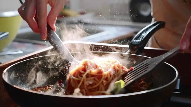 Cooking and stirring the spaghetti with red tomato sauce in the frying pan.