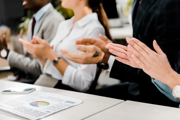 partial view of multiracial businesspeople applauding to speaker in office