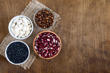 Assortment of colorful raw beans in bowls on a wooden table. Healthy food, dieting, nutrition concept. Legumes - vegan protein source.