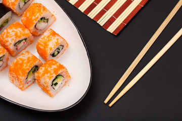Uramaki California. Sushi rolls, wooden napkin and sticks on black background.
