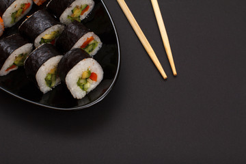Sushi rolls in nori seaweed sheets and soy sauce on black background.