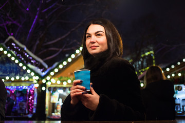 Beautiful adult girl with cup of hot drink at Christmas fair in Lviv, Ukraine.