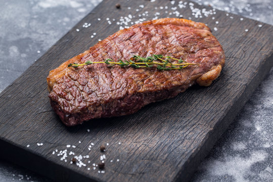 Raw ribeye beef steak cooking on black board with salt and rosemary