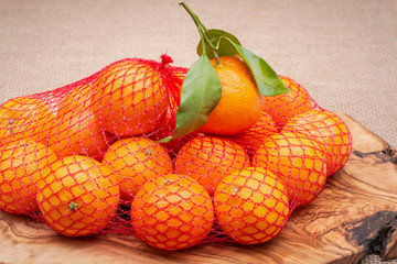 Fresh ripe organic mandarins in plastic mesh sack on olive wood and burlap background.
