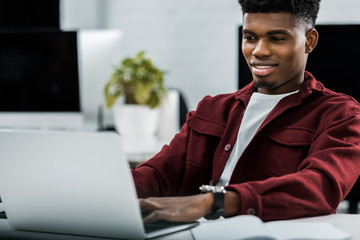 portrait of smiling african american businessman working on laptop in office