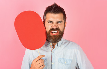 Angry bearded man hold paper nameplate. Feeling&emotions. Face expression. Fashion, beauty, hairdressing, barber salon. Wrathful man with beard&mustache. Red blank paper. Evil man with empty name card