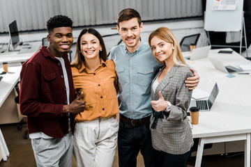 portrait of young happy multiracial business colleagues showing thumbs up in office