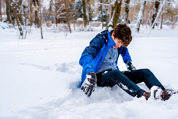Fototapeta na wymiar young boy teenager sitting on the snow ground in the winter park f