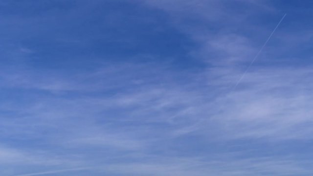 This is footage of plane flying by over the blue sky with some clouds arround it. The plane leaves a vapour trail.