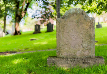 Fototapeta na wymiar A worn sandstone grave marker in the shade on a very day. There is no text visible on the stone, but there is some moss on the top.