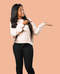 Young afro american woman holding copyspace imaginary on the palm to insert an ad on isolated brown...