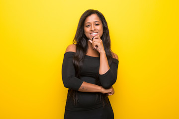 Young afro american woman on vibrant yellow background smiling and looking to the front with confident face