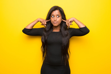Young afro american woman on vibrant yellow background covering both ears with hands - obrazy, fototapety, plakaty