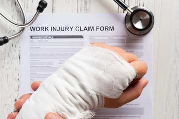 man holding his wrapped hand on top of a work injury claim form with stethoscope  medical and...