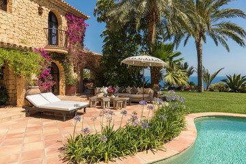 Luxurious summer or rest home with comfortable sofa and cushions in front of the pool with a lovely garden