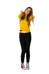 A full-length shot of a young girl with yellow sweater points finger at you while smiling on isolated white background