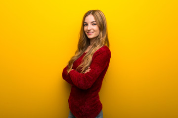 Young girl on vibrant yellow background keeping the arms crossed in lateral position while smiling