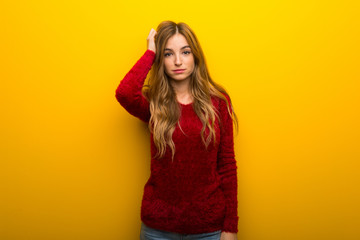 Young girl on vibrant yellow background with an expression of frustration and not understanding