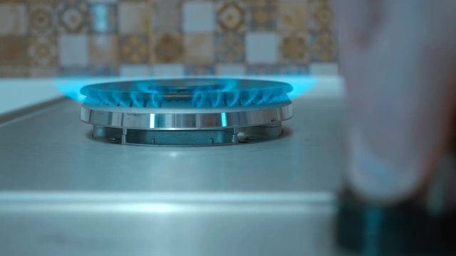 Gas igniting on the stove in the kitchen. Fingers turn the gas valve. Quick heat plate. Burner with double crown of burning gas