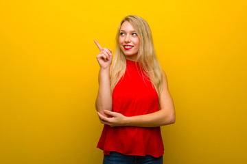 Young girl with red dress over yellow wall pointing a great idea and looking up