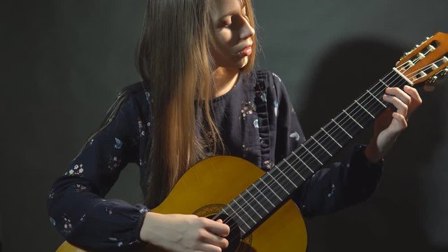 Girl play guitar. Studio light. Dark background.
