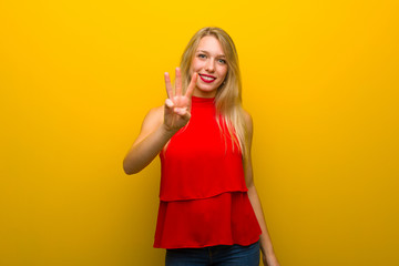 Young girl with red dress over yellow wall happy and counting three with fingers
