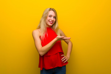 Young girl with red dress over yellow wall presenting an idea while looking smiling towards