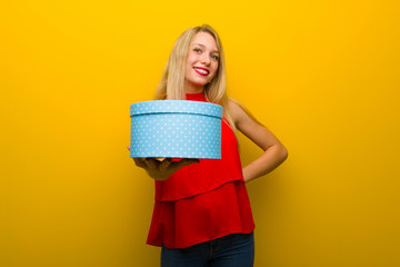 Young girl with red dress over yellow wall holding a gift in hands