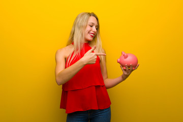Fototapeta na wymiar Young girl with red dress over yellow wall holding a piggybank
