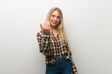 Blonde young girl over white wall inviting to come with hand. Happy that you came