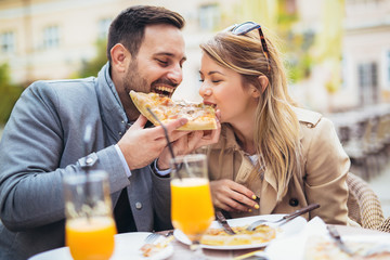 Beautiful loving couple sitting in outdoor cafe and eating pizza.