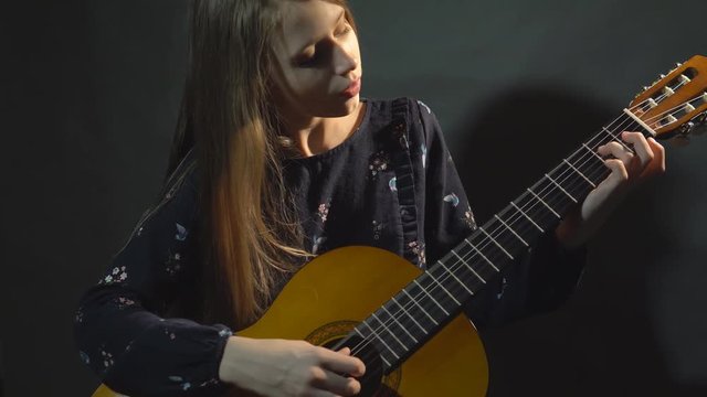 Girl play guitar. Studio light. Dark background.
