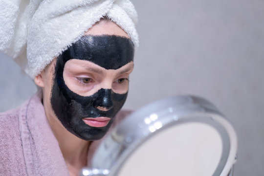 Young girl in a cleansing black coal mask on her face. Black coal exfoliating mask for the face. Black mask deep cleansing. Peel off face mask, blackhead removal.