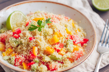 Couscous salad with fresh red and yellow bell peppers, avocado, tomatoes and lime. The concept of vegan and healthy food.