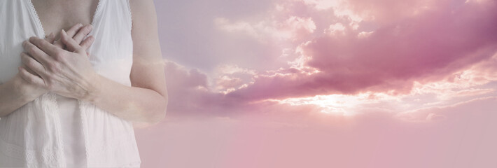 True Compassion from my Heart - female in white tunic with hands crossed over heart fading into a beautiful gentle pink clouded sun set with copy space on right side
 - obrazy, fototapety, plakaty