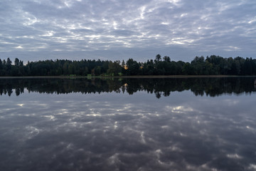 blue sky, clouds and trees from forest reflecting in calm lake water