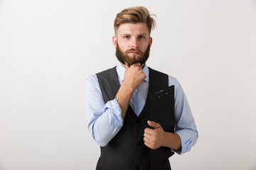 Handsome young bearded man standing isolated over white wall background holding clipboard.