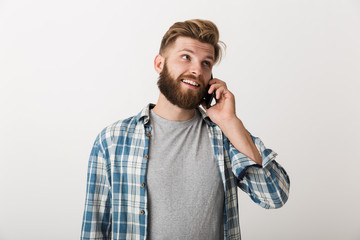 Handsome young bearded man standing isolated over white wall background talking by mobile phone.