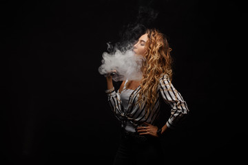 Redhead woman vaping electronic cigarette with smoke on black background closeup. Young woman...