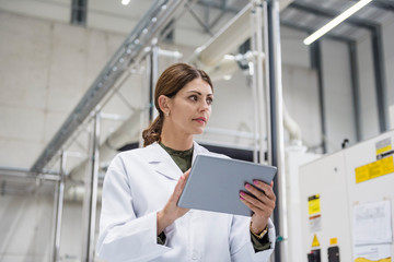 Woman checking manufacturing machines in high tech company, using digital tablet