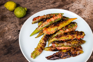 Stuffed peppers with a large number of burners on a white ceramic plate, viewed from the top, were placed on old brown wooden plates with charcoal stains. The green kaffir lime paste