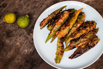 Stuffed peppers with a large number of burners on a white ceramic plate, viewed from the top, were placed on old brown wooden plates with charcoal stains. The green kaffir lime