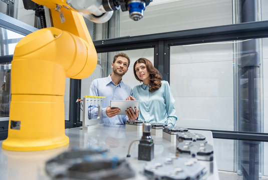 Colleagues In High Tech Company Controlling Industrial Robots, Using Digital Tablet