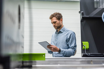 Businessman in high tech company controlling manufacturing machines, using digital tablet