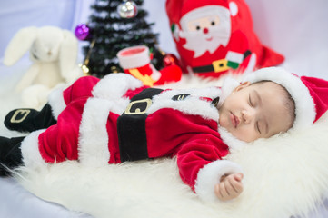 Fototapeta na wymiar little baby wearing Santa Claus costume sleep on white fur carpet with Christmas tree. Concept of celebrates Christmas and New Year's holidays.