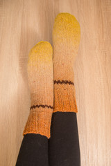 A woman wearing warm hand craft socks. Knitted from a natural sheep wool yarn. Winter clothing. On a wooden background.